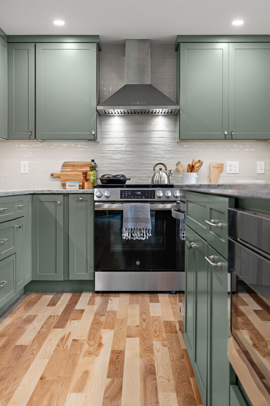 Green kitchen cabinets with island seating and light brown wood floors.