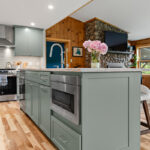 Green kitchen cabinets with island seating and light brown wood floors.