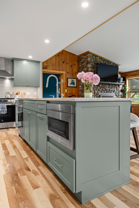 Green kitchen cabinets with island seating and light brown wood floors.