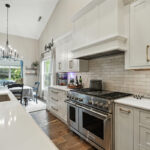 White kitchen cabinets with wood hood and stainless-steel professional oven.