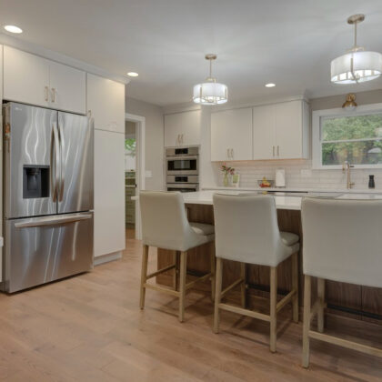 White painted kitchen cabinets with island seating and stainless steel fridge