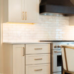 Light Mocha painted perimeter kitchen cabinets and an island with dark stained hood and island.