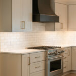 Light Mocha painted perimeter kitchen cabinets and an island with dark stained hood and island.