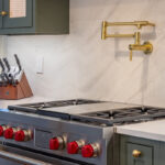 Green painted kitchen cabinets on each side of a a stainless steel stove with kettle faucet above.