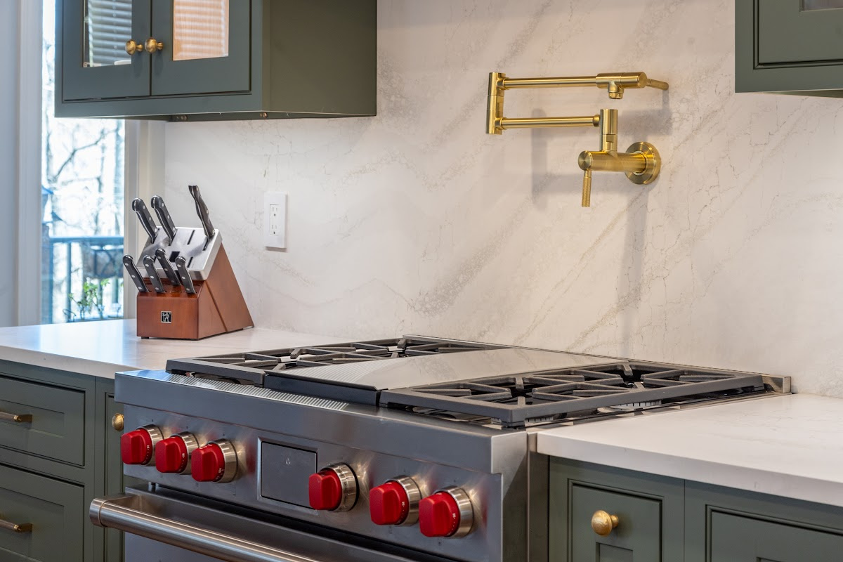 Green painted kitchen cabinets on each side of a a stainless steel stove with kettle faucet above.