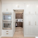 Beige painted tall cabinets with walk in pantry door open looking into a brown stained pantry