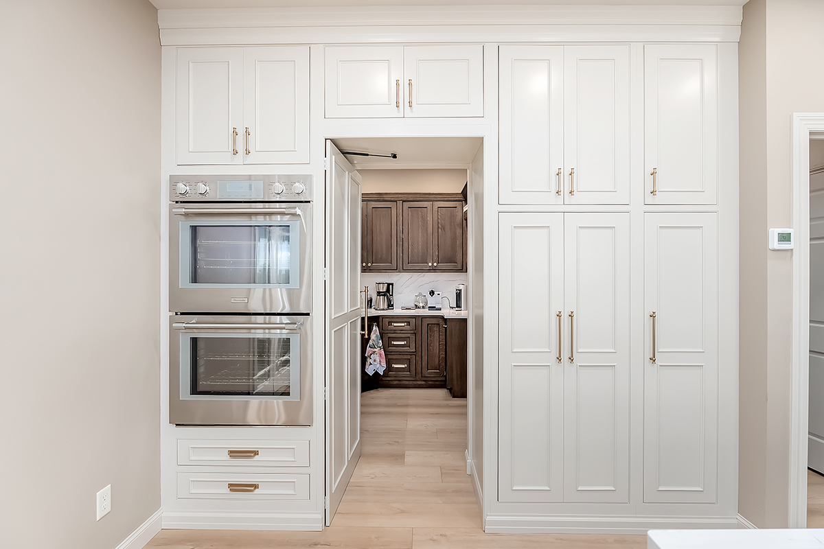 Beige painted tall cabinets with walk in pantry door open looking into a brown stained pantry