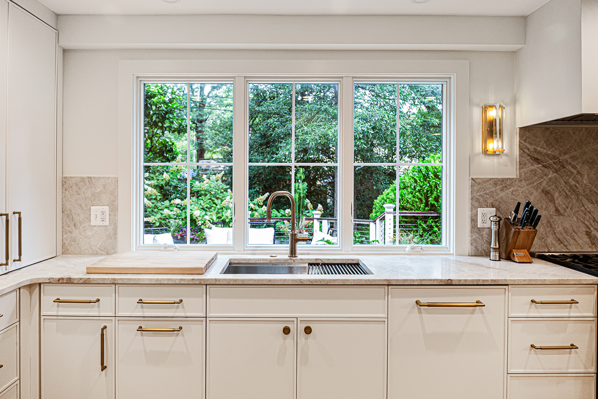 White painted kitchen cabinets with sink view out of a large window.