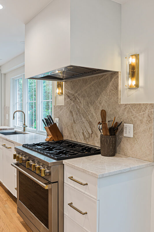 White painted kitchen cabinets and large hood above stove.