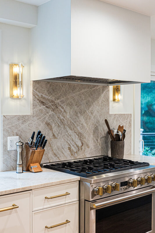 White painted kitchen cabinets and large hood above stove.