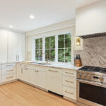White painted kitchen cabinets with sink view out of a large window. Shows professional stainless steel stove.