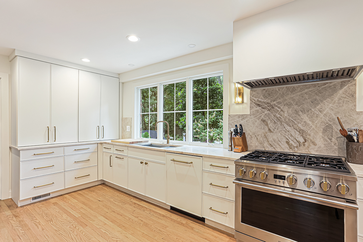White painted kitchen cabinets with sink view out of a large window. Shows professional stainless steel stove.