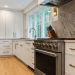 White painted kitchen cabinets with sink view out of a large window. Shows professional stainless steel stove.