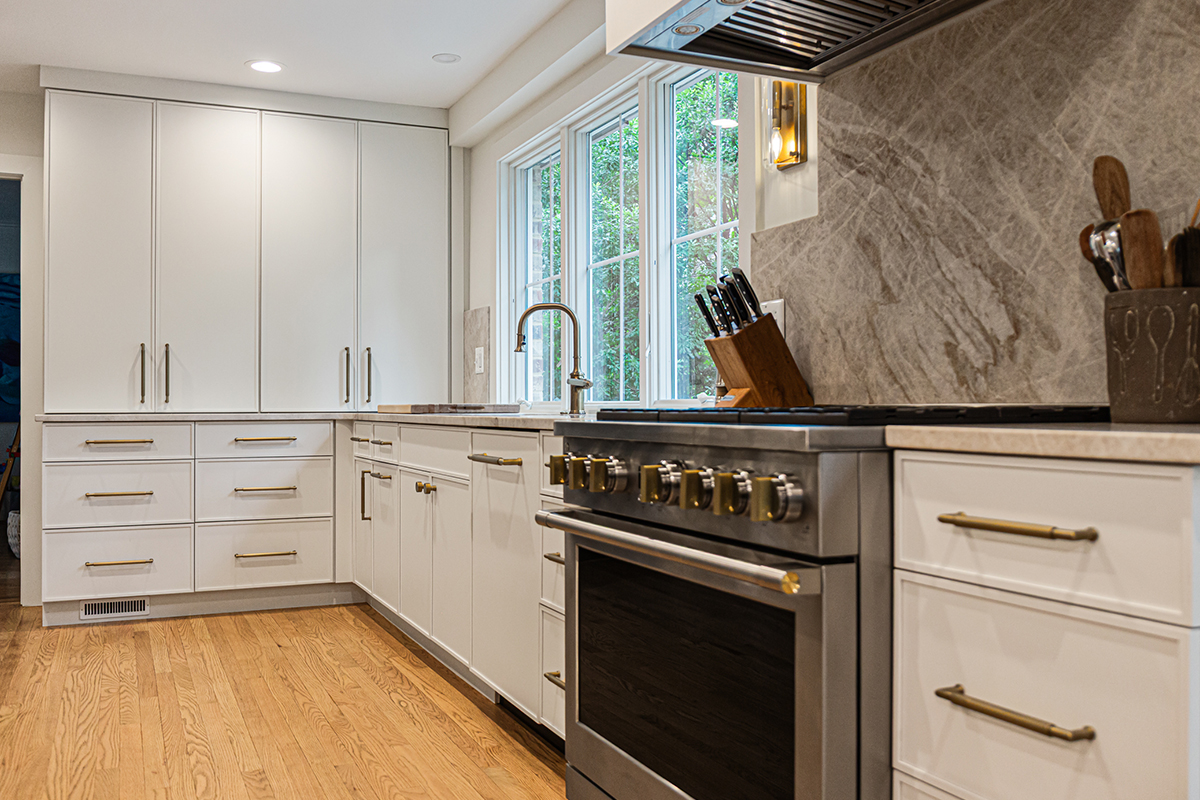 White painted kitchen cabinets with sink view out of a large window. Shows professional stainless steel stove.