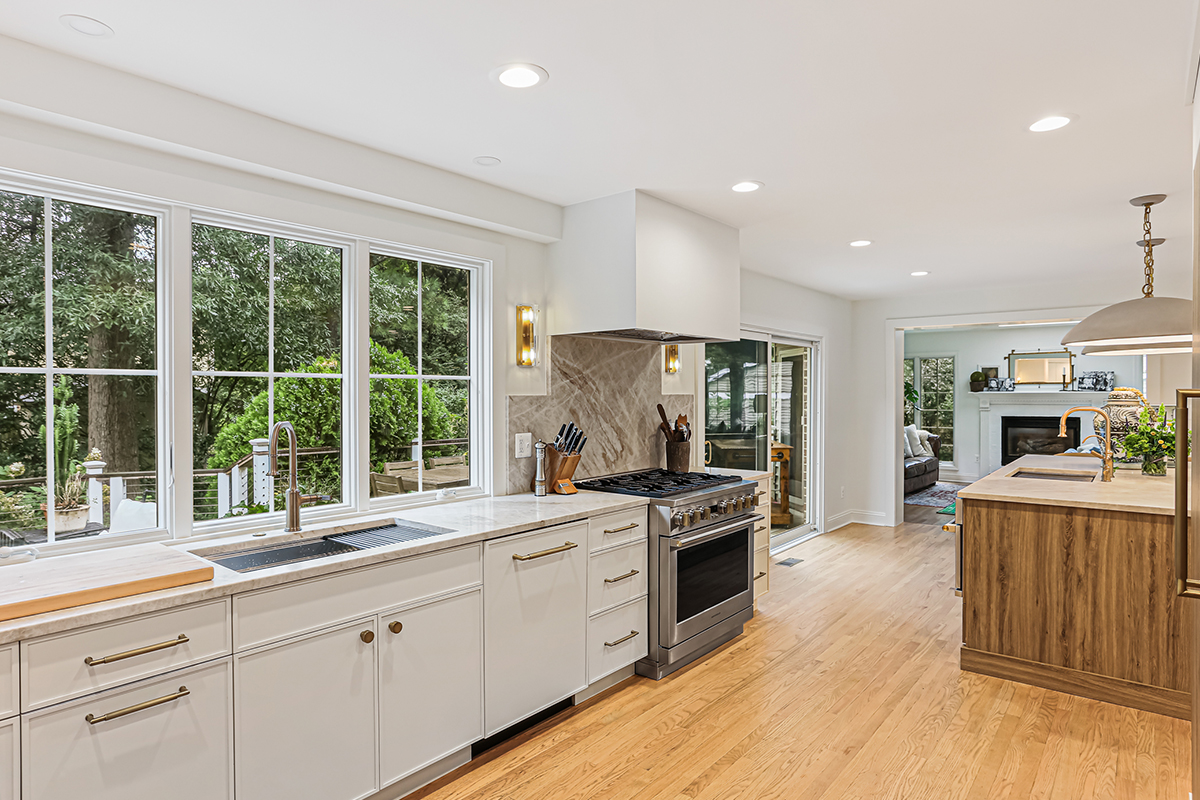 White painted kitchen cabinets with sink view out of a large window. Shows professional stainless steel stove.